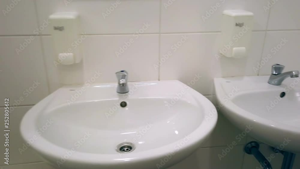 Filming womens toilet with white sinks and wall mounted soap containers. Public toilet with white ceramic tiles and separated male and female part. Filming womens toilet with white sinks and wall mounted soap containers. Public toilet with white ceramic tiles and separated male and female part.