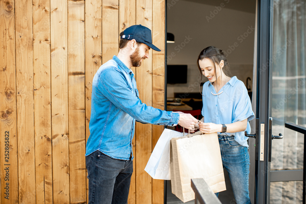 Delivery man bringing some goods packaged in paper bags for a young woman client to home. Buying clothes online and delivery concept Delivery man bringing some goods packaged in paper bags for a young woman client to home. Buying clothes online and delivery concept