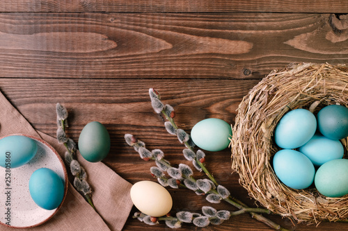 Bird nest with turquoise easter eggs and  pussy willow branch on wooden desk. Flat lay easter composition, above view photo