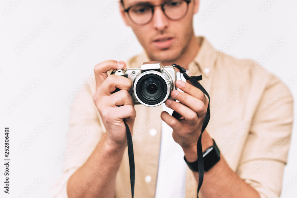 Young man taking photo on digital camera, posing over white studio background. Young male wearing casual outfit and trendy eyewear, blogging and looking to the camera display. Young man taking photo on digital camera, posing over white studio background. Young male wearing casual outfit and trendy eyewear, blogging and looking to the camera display.
