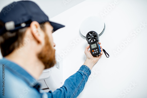 Handyman checking the speed of air ventilation with measuring tool on the white wall background photo