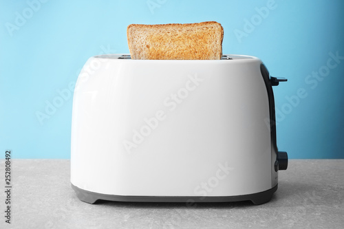 Slice of bread with toaster on table against color background
