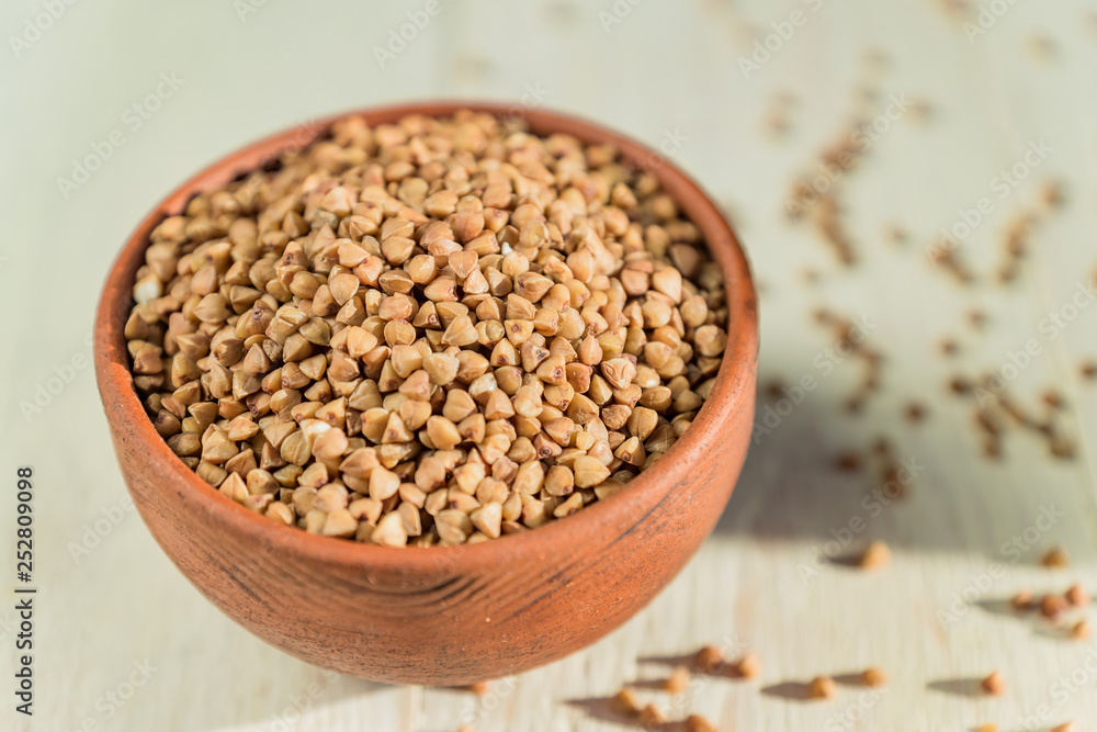 Dry buckwheat in brown clay bowl on wooden table. gluten free grain for healthy diet