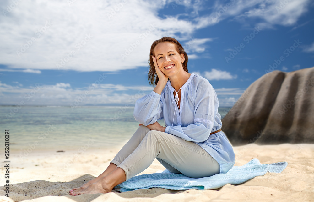 people and summer concept - happy smiling woman sitting on towel over seychelles island tropical beach background