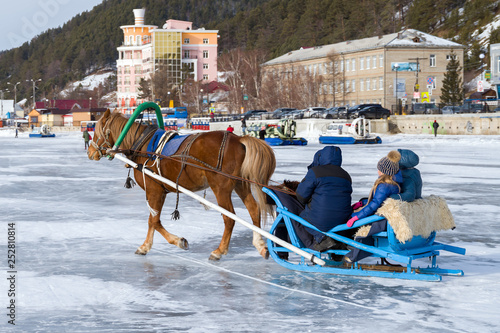 A horse harnessed to a sleigh rides tourists on the ice of Lake Baikal. Listvyanka, Siberia, Russia 