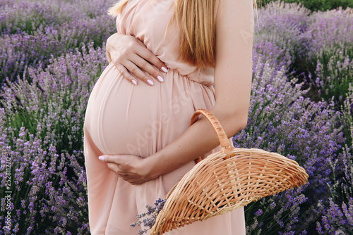 Pregnant girl blonde in a beige dress and straw hat. Lavender field. In anticipation of a child. The idea of a photo shoot. Walk at sunset. Future mom. Basket of flowers.