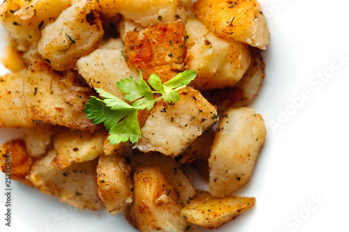 Delicious gold fried potato with herbs on big rounded white plate. Tasty rustic dish for dinner on white background.