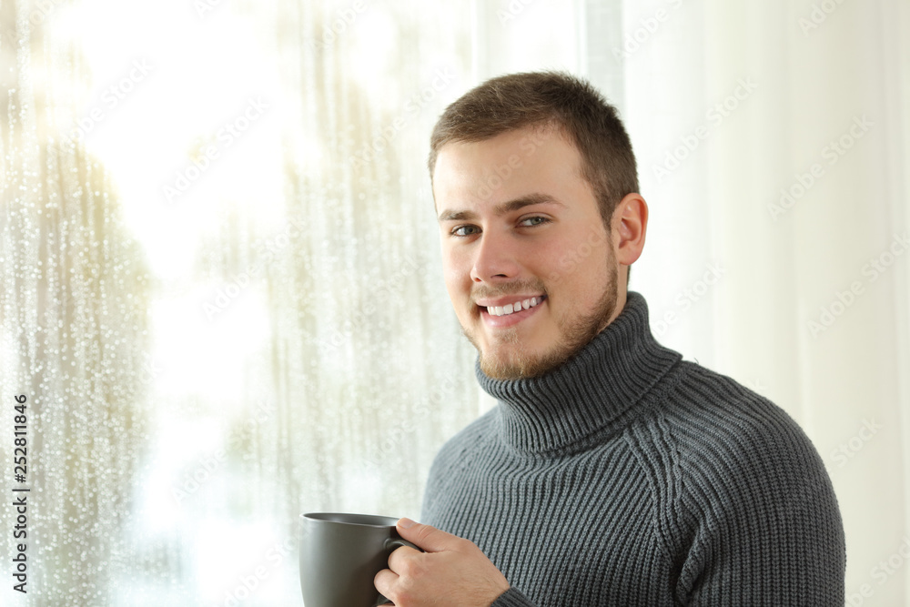 Happy tenant looking at camera beside a window at home Happy tenant looking at camera beside a window at home