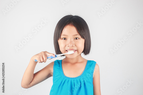 Cute little Asian girl brushing her teeth on gray background