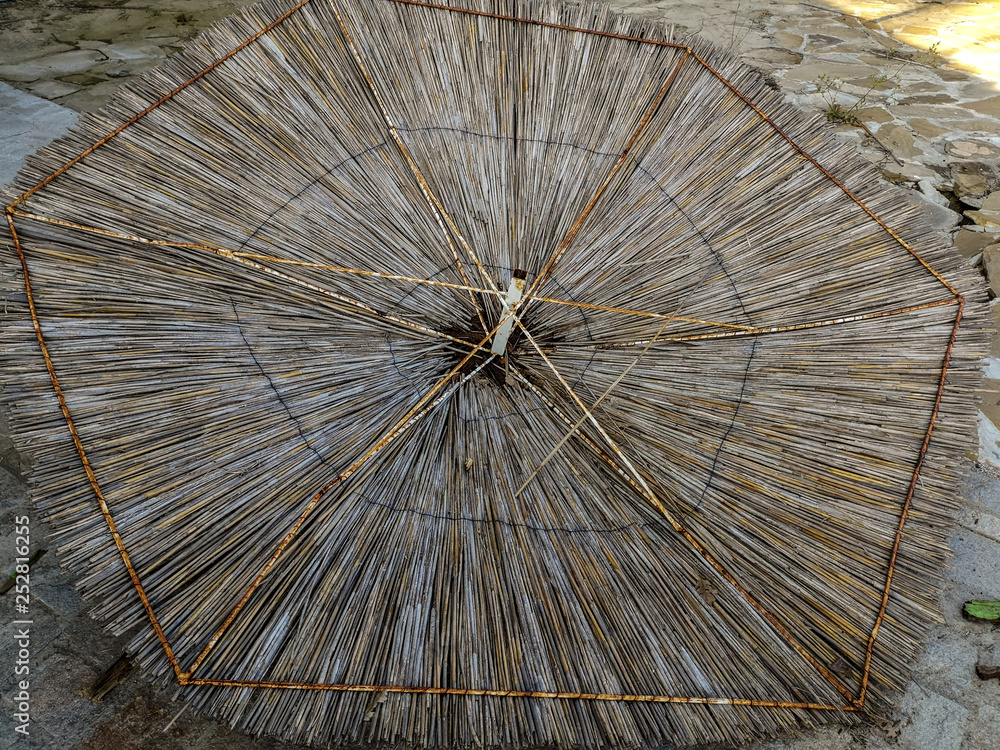 Thatched roof in the shape of an umbrella with rusty spokes lying on the floor