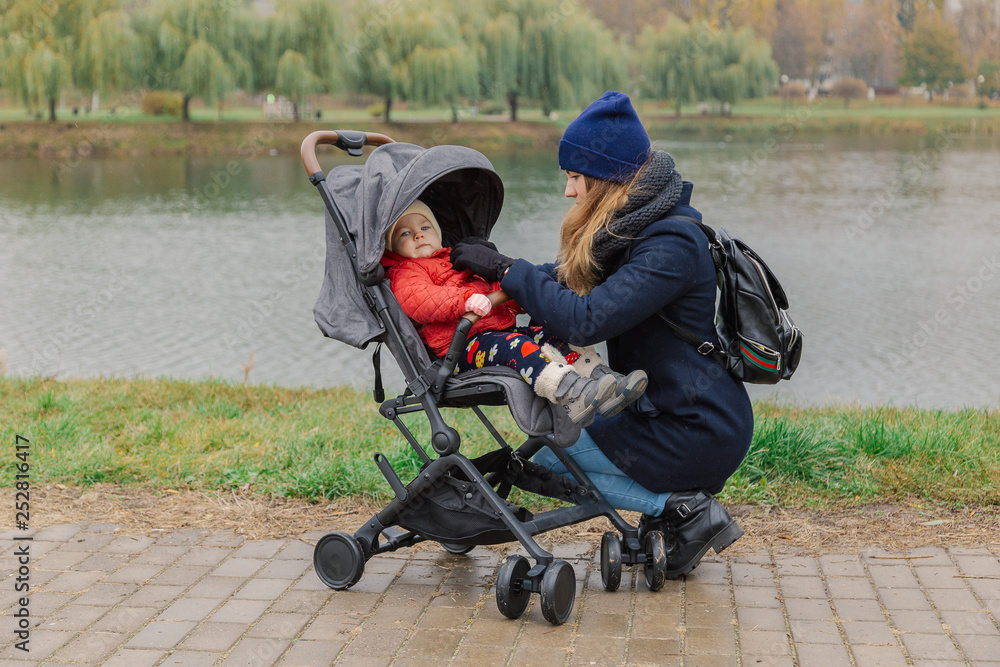 A woman walks in the park with a stroller and a small child near the lake. A woman walks in the park with a stroller and a small child near the lake.