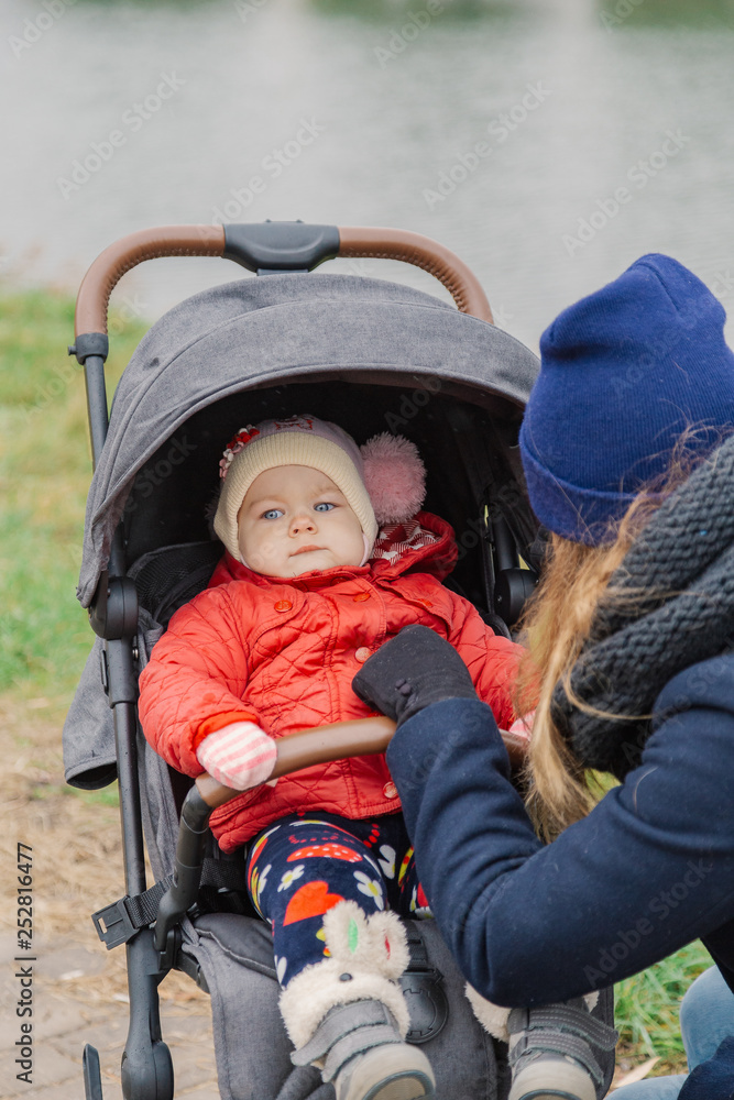 A woman walks in the park with a stroller and a small child near the lake. A woman walks in the park with a stroller and a small child near the lake.