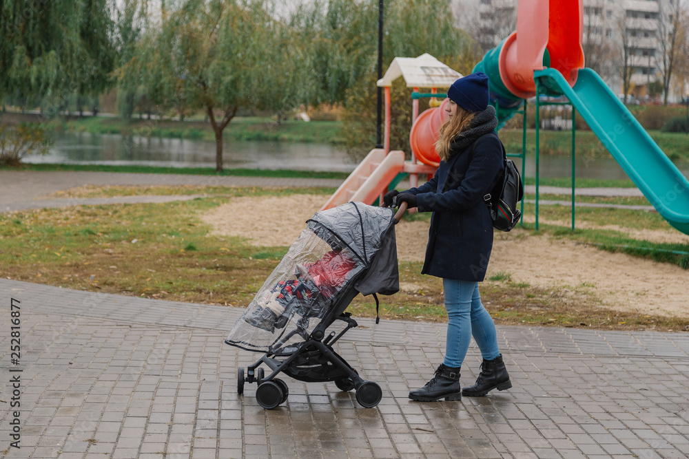 A woman walks in the park with a stroller and a small child.