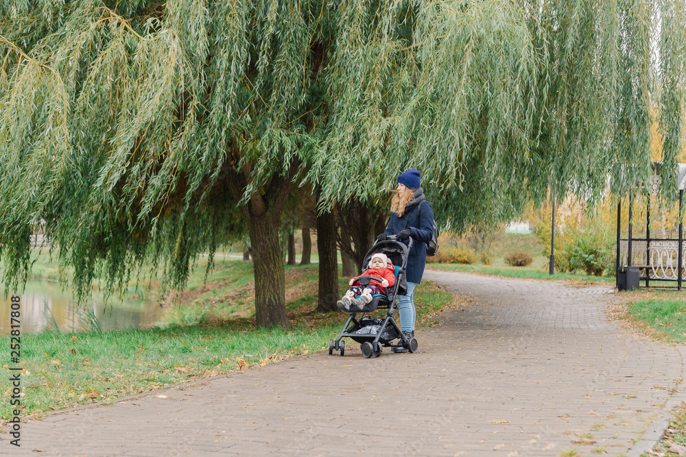 Obraz premium A woman walks in the park with a stroller and a small child.