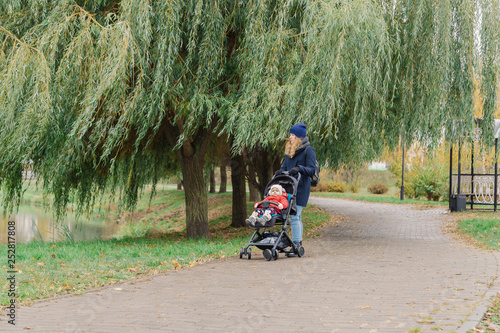 Fototapeta Naklejka Na Ścianę i Meble -  A woman walks in the park with a stroller and a small child.