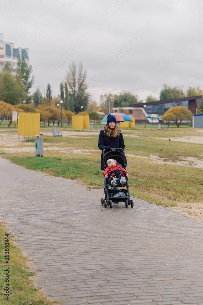 Obraz premium A woman walks in the park with a stroller and a small child near the lake.