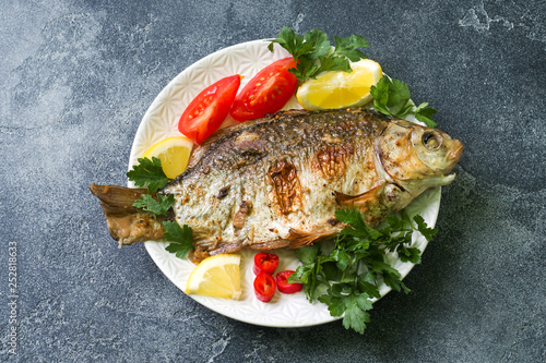 Baked carp fish with vegetables and spices on a plate on a dark table with a copy of space.