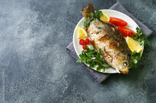Baked carp fish with vegetables and spices on a plate on a dark table with a copy of space.