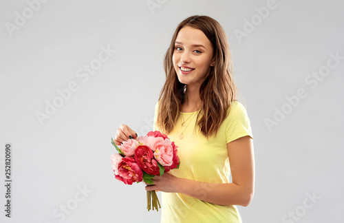 birthday and people concept - smiling young woman or teenage girl in yellow t-shirt with flower bouquet over grey background