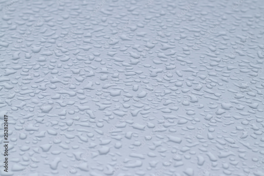 View of the big raindrops on the roof of a light blue car View of the big raindrops on the roof of a light blue car
