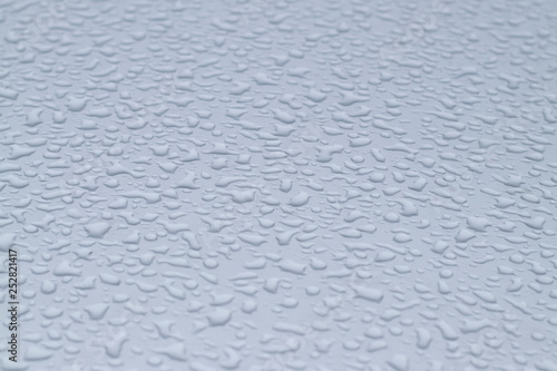 View of the big raindrops on the roof of a light blue car