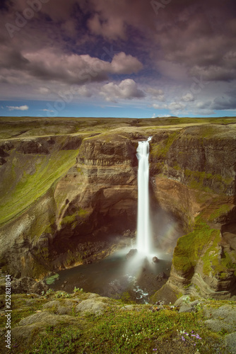 The Haifoss Waterfall with golden clouds in the sky. The flowing water is captured by a long exposure. Amazing blue color of water from the glacier. Natural and colorful environment...