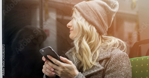 Happy female passenger listening to music on a smartphone in public transportation.