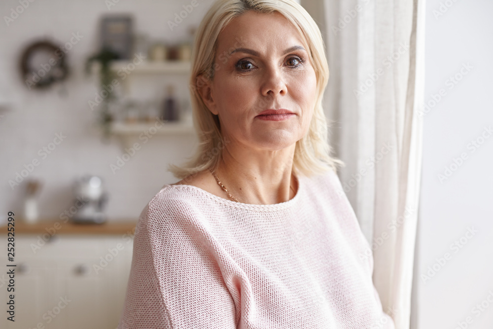 Beauty, aging, people and lifestyle concept. Horizontal image of gorgeous positive middle aged European female with blonde hair and natural make up spending day at home, smiling joyfully at camera Beauty, aging, people and lifestyle concept. Horizontal image of gorgeous positive middle aged European female with blonde hair and natural make up spending day at home, smiling joyfully at camera
