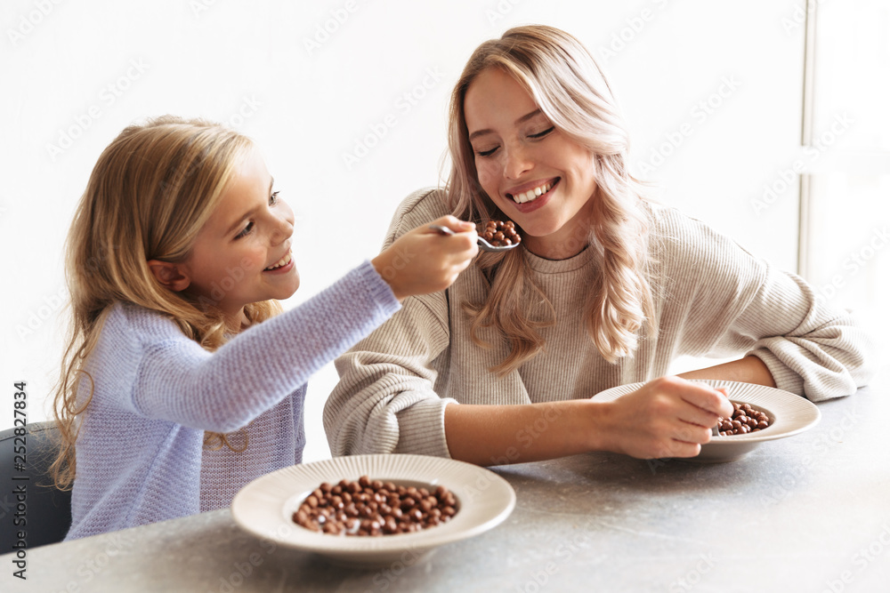 Two happy girls sisters at kitchen indoors eat have a breakfast together. Two happy girls sisters at kitchen indoors eat have a breakfast together.