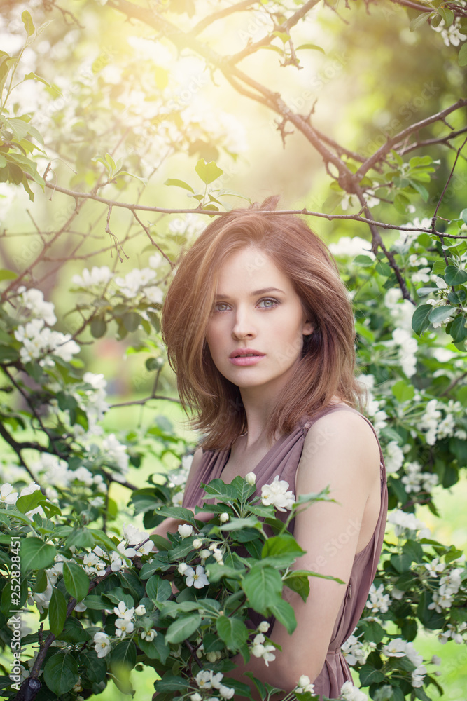 Natural beauty. Beautiful female model girl with brown hair in spring blossom park. Young perfect woman on spring flowers background Natural beauty. Beautiful female model girl with brown hair in spring blossom park. Young perfect woman on spring flowers background