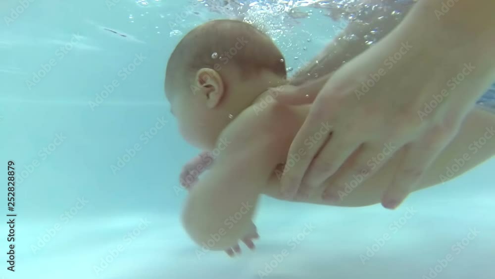 Vidéo Stock Newborn baby swimming in the bath or bathtub. Mother help him swim. Mom teaches baby