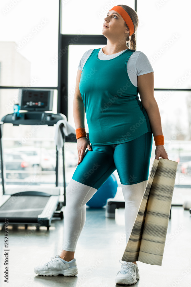 attractive overweight woman holding fitness mat in gym