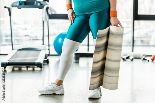 cropped view of overweight woman holding fitness mat in gym