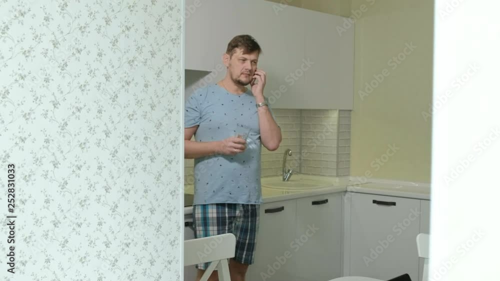 A man in pajamas drinking water in the kitchen. Morning A man in pajamas drinking water in the kitchen. Morning