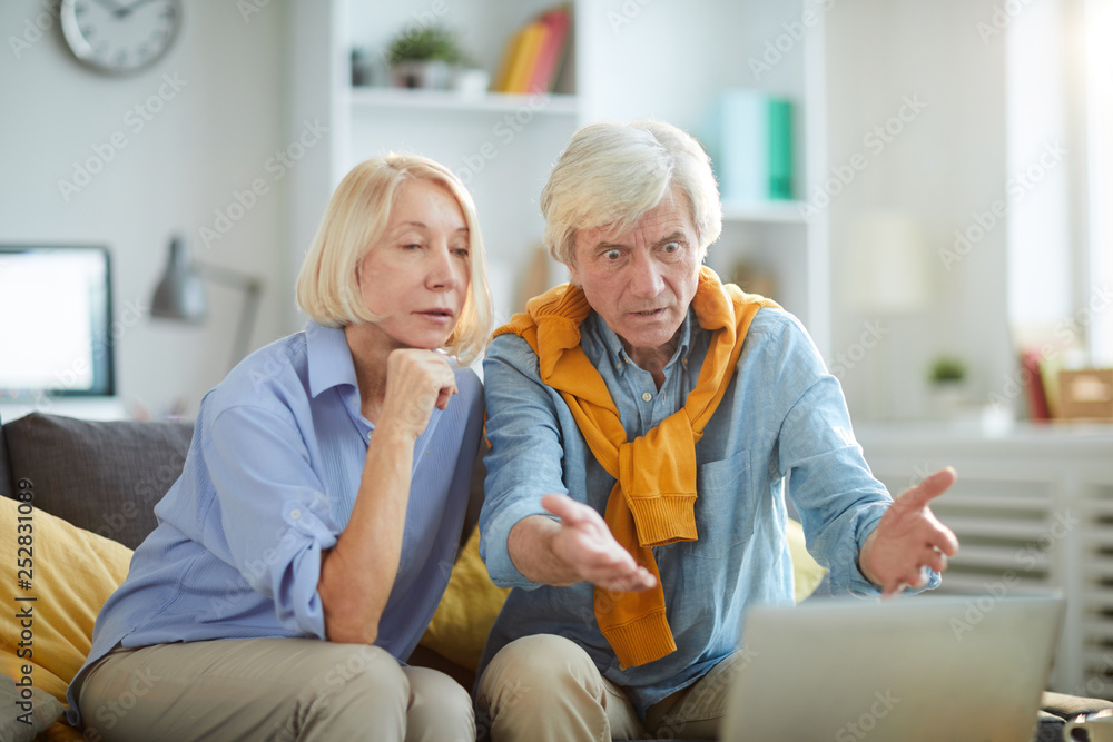 Portrait of shocked senior man looking at computer screen while using laptop at home, copy space Portrait of shocked senior man looking at computer screen while using laptop at home, copy space