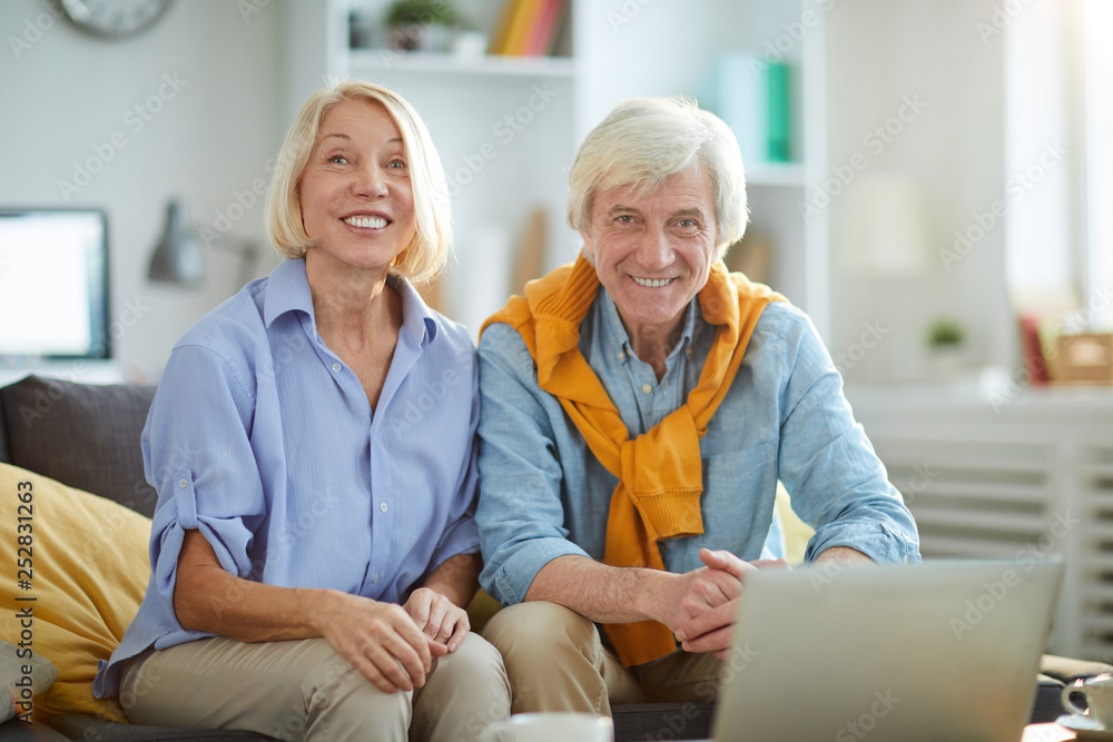 Portrait of contemporary senior couple sitting on sofa at home and looking at camera, copy space Portrait of contemporary senior couple sitting on sofa at home and looking at camera, copy space