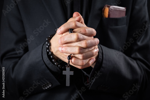 Christian person praying, low key image. Hands of a man in black suit or a priest portraying a preach