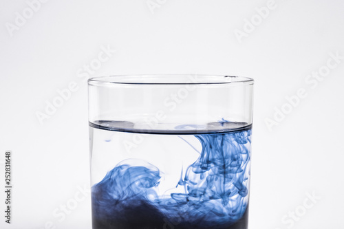Water contamination concept. Dark substance dissolving with clean water in a glass in white background, close-up view