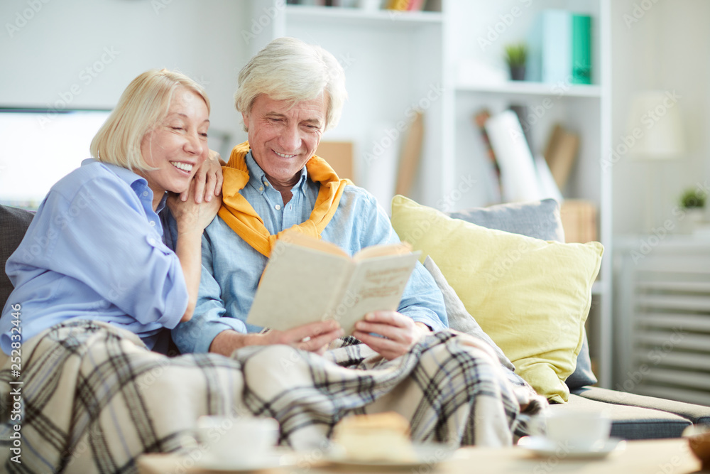 Portrait of happy mature couple reading book together sitting on couch at home, copy space Portrait of happy mature couple reading book together sitting on couch at home, copy space