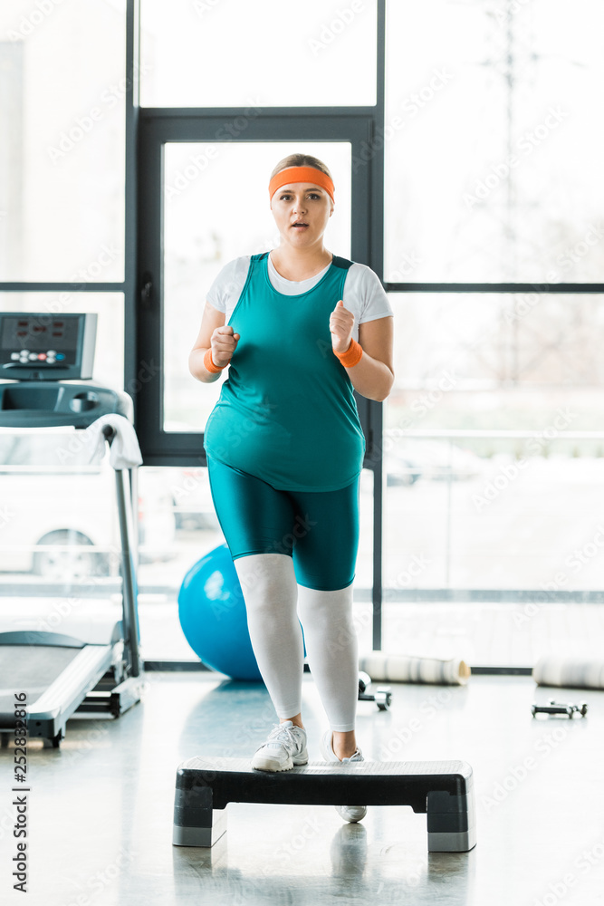 Fototapeta premium overweight girl exercising on step platform near sport equipment