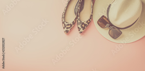 Straw hat, sunglasses and trendy leopard print shoes on pastel pink background, summer fashion concept. Top view, selective focus