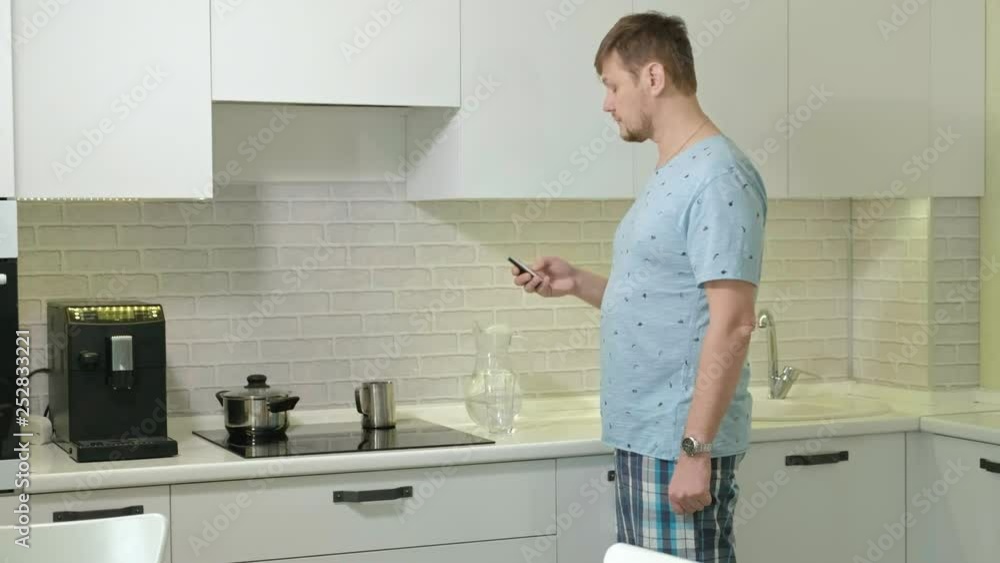 A man in pajamas drinking water in the kitchen. Morning A man in pajamas drinking water in the kitchen. Morning