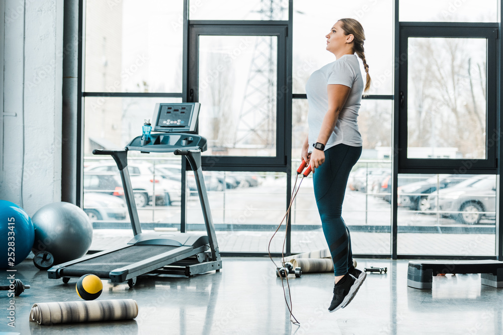 Fototapeta premium attractive plus size woman exercising with jumping rope in gym