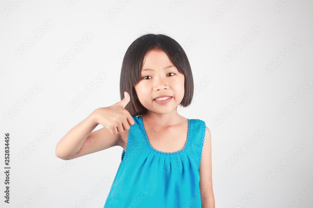 Cute little asian girl giving thumb up hand sign on gray background Cute little asian girl giving thumb up hand sign on gray background