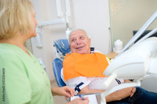 Smile senior male patient in dental chair have dialog with female dentist. Dental care for elder people. Dentistry, medicine and health care concept
