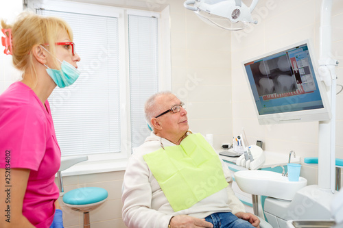 Senior man 75 years old on a review of a dentist, sitting in a chair. Dentist female explaining X-Ray to older man. Dental care for older people. Dentistry, medicine and health care concept
