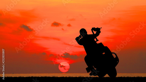 Silhouette biker with his motorbike beside the natural lake and beautiful sunset sky.