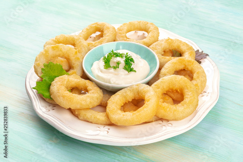 A closeup of a plate of calamari rings with a mayonnaise dip