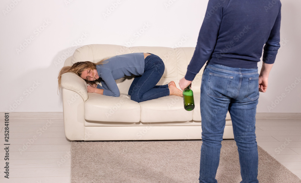 People, violence and abuse concept - Man drinking alcohol while wife is lying on sofa People, violence and abuse concept - Man drinking alcohol while wife is lying on sofa