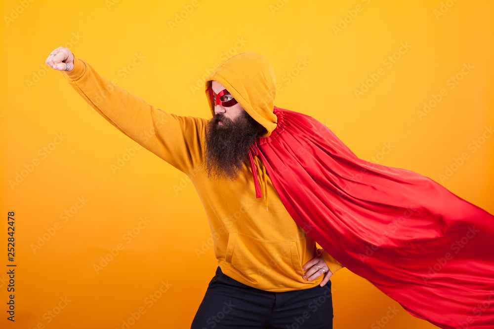 Fototapeta Superhero with red cape and mask flying away in studio over yellow background
